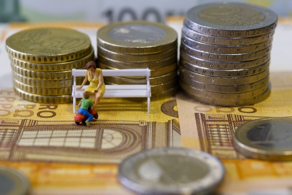 Moedas e notas de euros, mulher sentada em banco de jardim com criança.