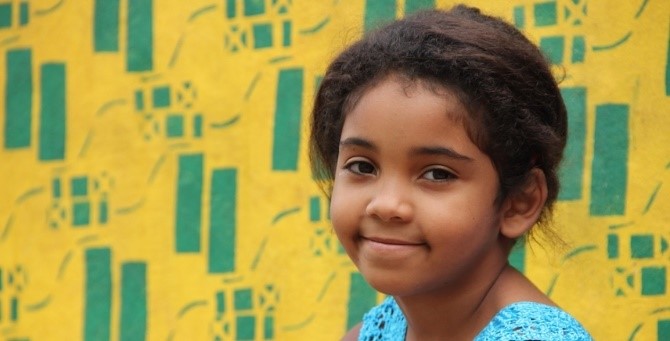 Foto de criança a sorrir em fundo amarelo e verde.