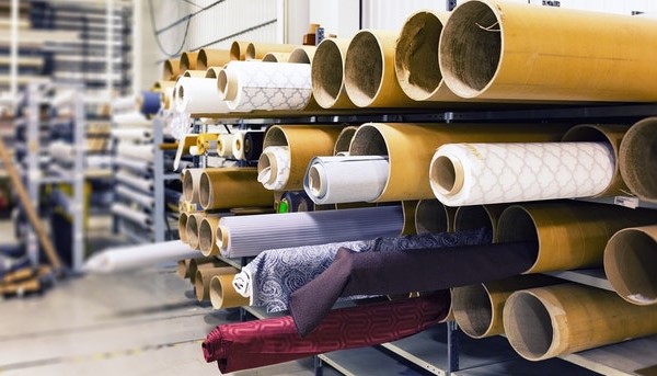 Imagem de fábrica têxtil onde se podem visualizar vários rolos de tecidos.