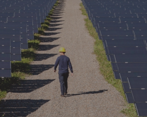Trabalhador a caminhar num estrada de campo com painéis solares de ambos os lados.