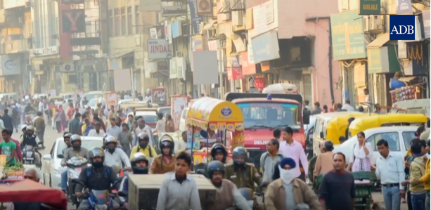 Rua em Nova Deli (Índia). Pode visualizar-se uma mistura de pessoas, carros e motas na rua.