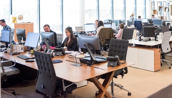 Sala de trabalho de uma empresa. Pode visualizar-se várias secretárias com computadores e os seus colaboradores.