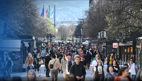 Aglomerado de pessoas a anda em rua rodeada de árvores e três bandeiras hasteadas ao fundo.