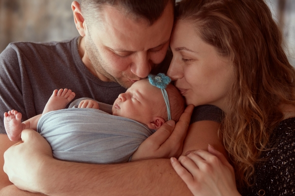 Pai e mãe abraçados à sua filha recém-nascida.