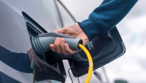 Homem a conectar o carregador a um carro elétrico na estação de carga