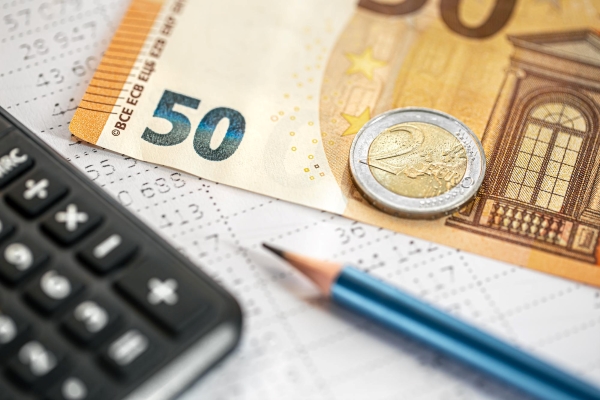 Calculadora, lápis, nota de 50 euros e moeda de 2 euros em fundo desfocado.