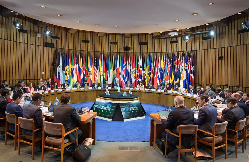 Sala da Assembleia, mesa redonda e bandeiras dos vários países.