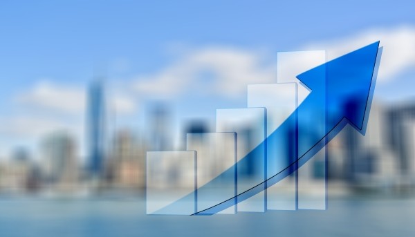 gráfico de barras crescente com seta ascendente; em fundo imagem de cidade desfocada